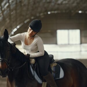 A woman riding a horse in an indoor equestrian arena, wearing a helmet.