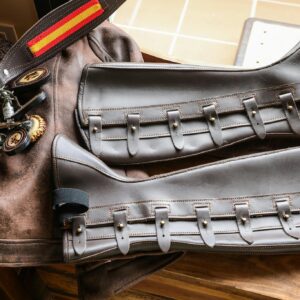 Close-up of leather equestrian gear including gaiters and saddle accessories on a wooden table.